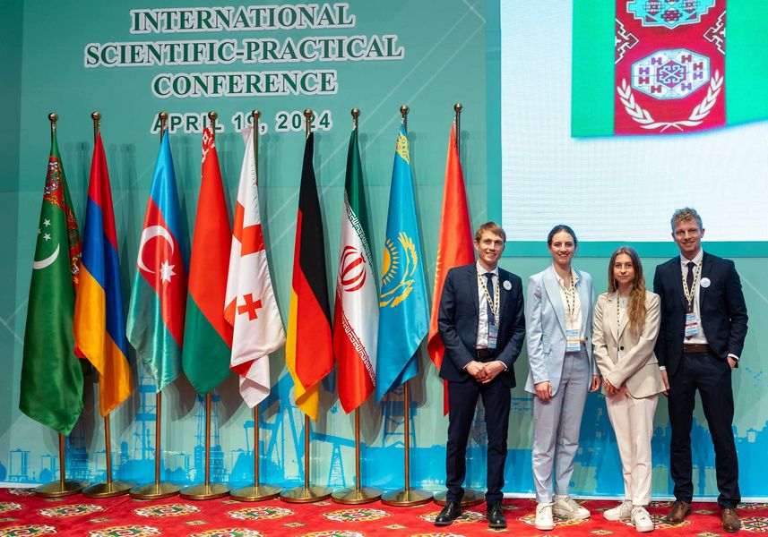 Eine Gruppe von vier Personen steht auf einem Podium, im Hintergrund die Flaggen verschiedener Länder. 