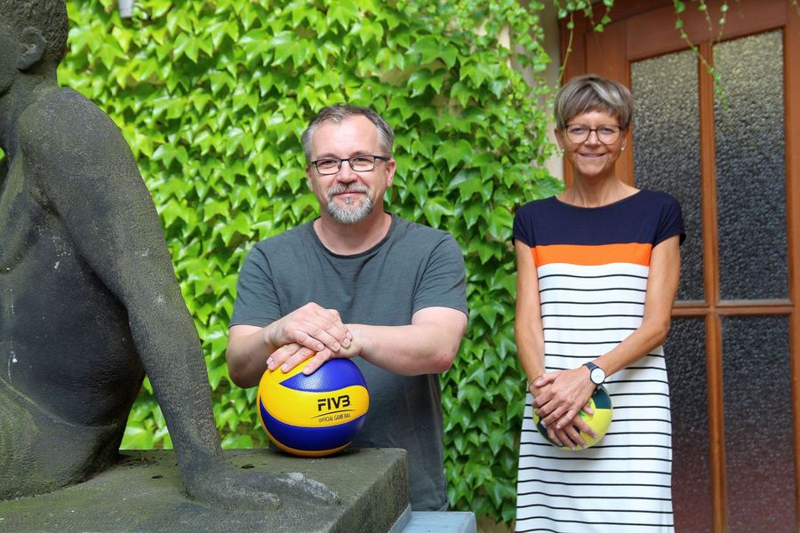 Foto: Zwei Beschäftigte des Hochschulsports der WHZ stehen vor einer berankten Wand. Holger Welt lehnt neben einer halb zu sehenden Skulptur auf einem Basketball, Ulrike Lemberg steht rechts hinter ihm mit einem Handball in den Händen.
