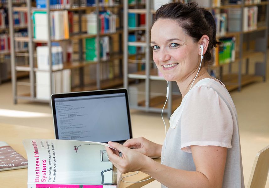 Studentin sitzt in Bibliothek vor einem Laptop und blättert in einem Buch (WHZ/Helge Gerischer)