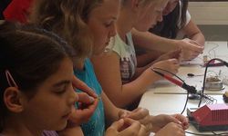 Foto: Mehrere Schülerinnen sitzen an einem Labortisch und betrachten in ihren Fingern ein Bauteil, welches Sie erklärt bekommen.