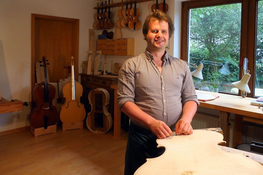 Ein Mann steht in einer Werkstatt, in der Musikinstrumente gefertigt werden. 