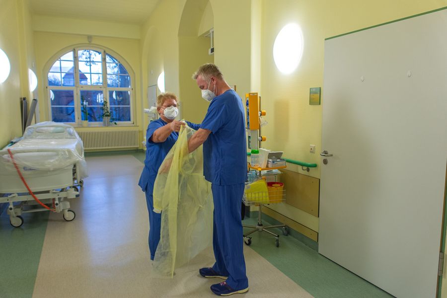Foto: Ein Krankenschwester legt Hr. Prof. Piehl einen Schutzkittel an. 