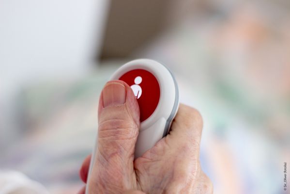 Symbolbild, Foto: Pflegezeit-Gesetze; Es ist die Hand einer älteren Person zu sehen, die einen Rufknopf für Pflegepersonal hält. (Quelle: Fotolia)
