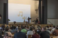 Foto: Zwei Personen auf der Aula Bühne Scheffelberg. Musikalische Eröffnung durch die Band SwingKONaction.