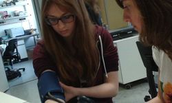 Foto: Zwei Schülerinnen. Eine Schülerin probiert ein Blutdruckmessgerät an ihrem Arm aus.