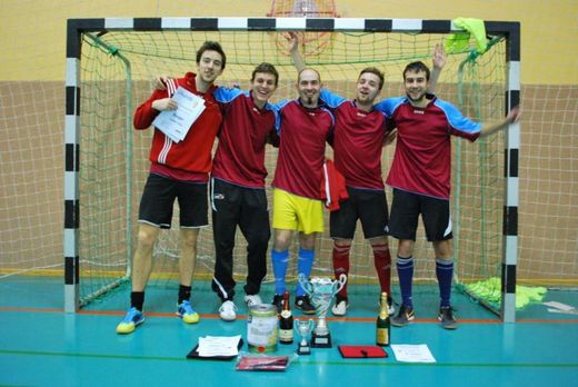 Foto: Gruppenbild einer 5 Personen Mannschaft vor einem Handballtor mit Urkunden und Siegerpokalen.