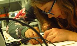 Foto: Eine Schülerin lötet unter Anleitung ein Bauteil in einem Elektrotechniklabor.