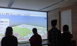 Foto: Schülerinnen betrachten auf einen an die Wand projizierten Bild eine topografische Karte in 3D.