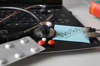 Foto: Ein Stethoskop, Tablettenpackung mit Pillen und ein Zettel mit der Aufschrift I VoTeG liegen auf einer Laptop Tastatur.