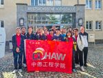 chinesische Studierende posieren mit einer Fahne der Deutsch-Chinesischen-Hochschule vor dem Haupteingang der WHZ.