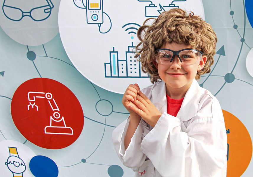 Junge im Kostüm eines Wissenschaftlers blickt in die Kamera. Im Hintergrund technische und wissescnhaftliche Symbole. 