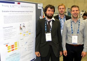 Foto: Drei Teilnehmer stehen neben einer Wand mit einem Plakat. Aufschrift: Evaluation of electroencephalography analysis methods.