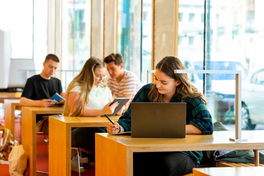 Studierende arbeiten in der Hochschulbibliothek an Tablets und Laptops. 