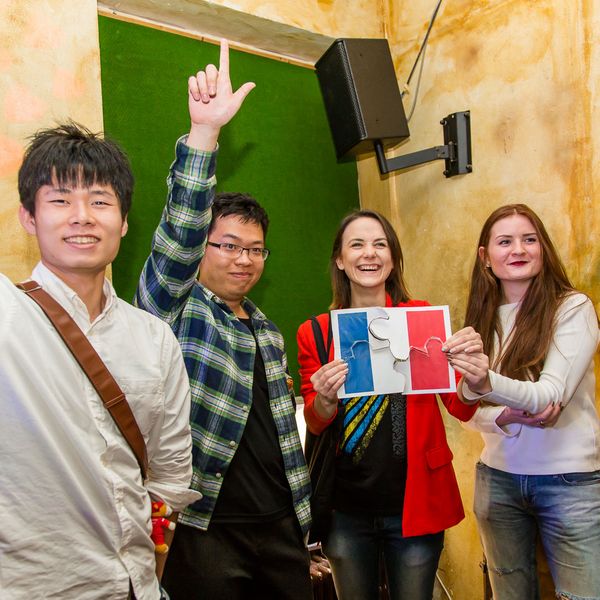 Foto: Vier Studierende stehen zusammen und halten ein Blatt mit einer Länderflagge.