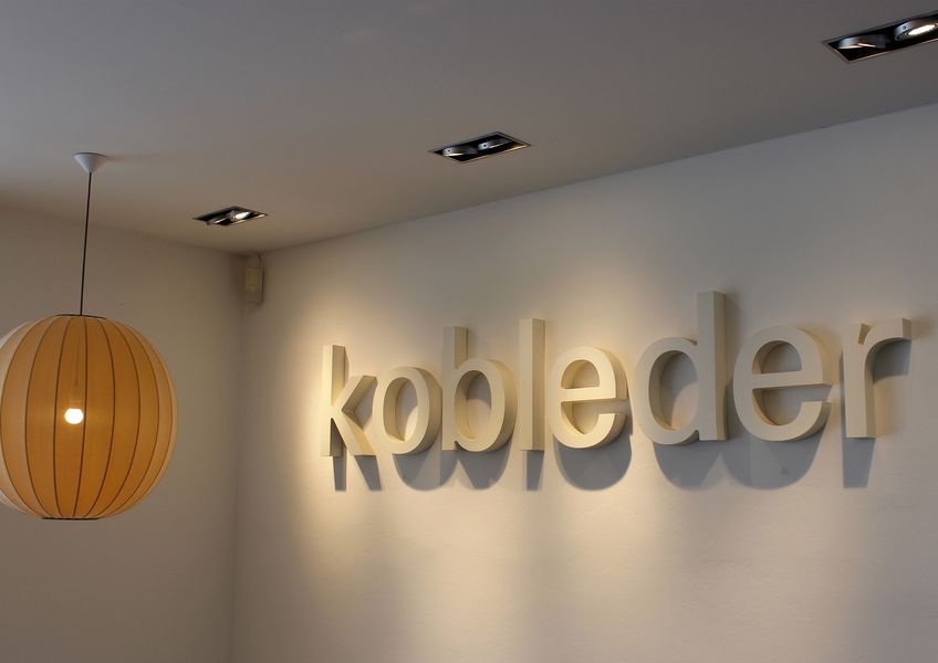 Foto: Ein Raum. Ein runder Lampenschirm hängt von der Decke. An der Wand eine Aufschrift mit dem Schriftzug "Kobleder".