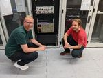 Foto: Zwei Männer hocken vor einem Supercomputer.