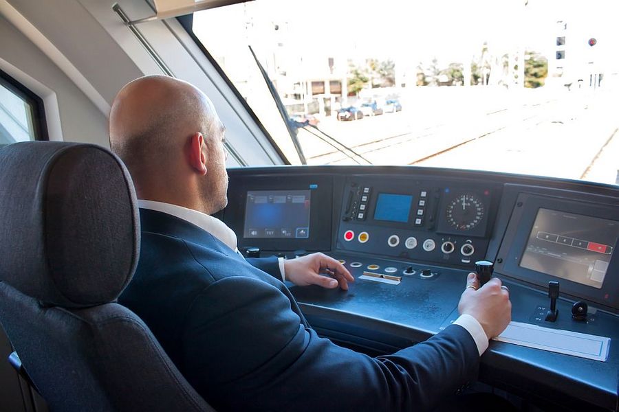 Foto: Ein Lokführer im Cockpit eines Zuges, Hand am Steuerhebel, Blick nach vorn. 