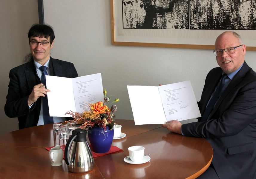 Foto: WHZ-Rektor Prof. Kassel links, Schulleiter Klaus-Peter Palme rechts, sitzen am Tisch, halten Urkunden in der Hand.