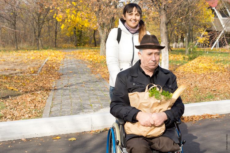 Symbolbild, Foto: Studieren mit Pflegeverantwortung; Eine junge Frau schiebt einen alten Mann im Rollstuhl, der eine Papiertüte mit Einkäufen in den Armen hält. (Quelle: Fotolia)