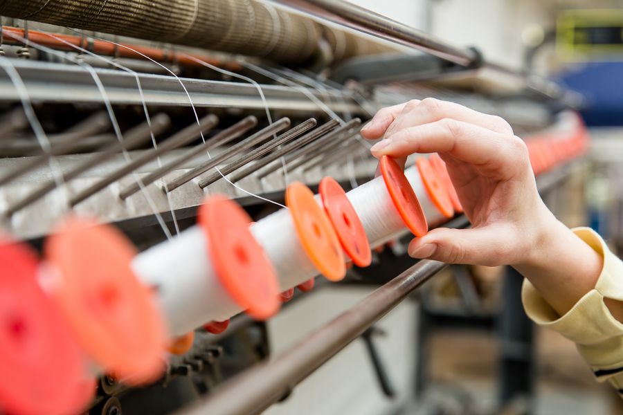 Foto: Ein Hand setzt eine Textilspindel in eine Maschine ein.