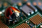 Foto: Rotes kybernetisches Insekt sitzt mit Chips und gelöteten Elementen auf der Hauptplatine der Computerhardware Quelle: oleksandr_info/Adobestock