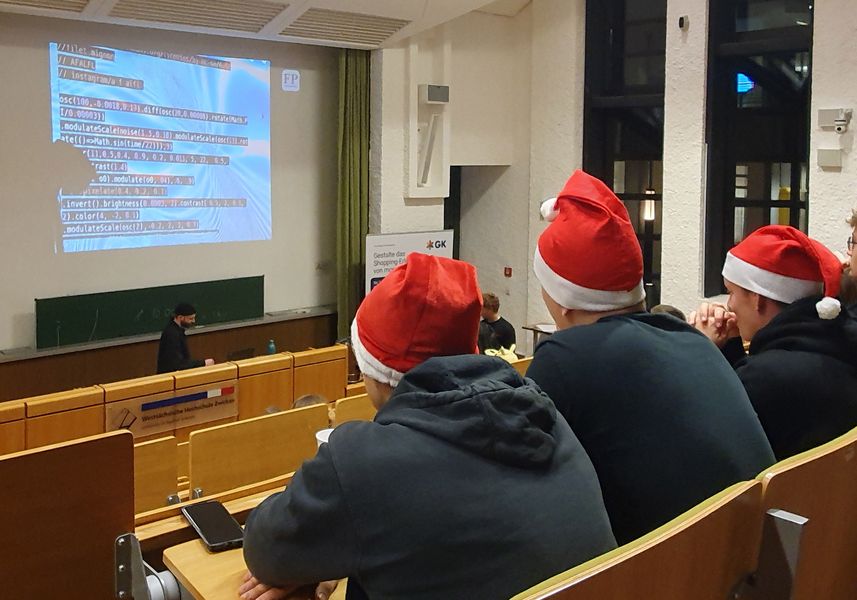Studierende mit Weihnachtsmützen verfolgen eine Vorlesung