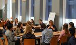 Foto: Studierende und Gäste sitzen in Gruppen in der Aula Scheffelberg und unterhalten sich.