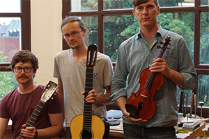 Foto: Drei Studierende mit zwei Gitarren und einer Geige in ihren Händen.
