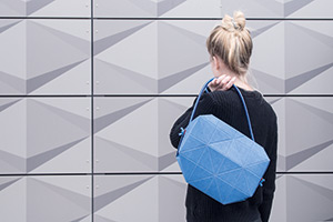 Foto: Ein Dame hat ihre Handtasche über der Schulter und betrachtet eine geometrisch strukturierte Wandverkleidung.