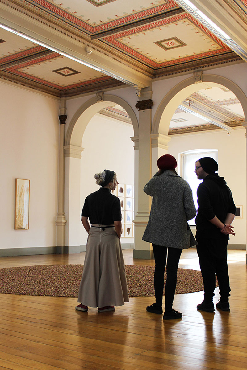 Foto: Drei Studierende stehen zur Exkursion in Altenburg in einem Ausstellungsraum und unterhalten sich.