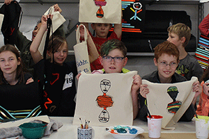 Gruppenbild: Kinder zeigen ihre gebastelteten, gemalten Motive auf Stoffbeuteln.