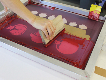 Foto: Eine Studierende in einem Atelier bringt Farbe beim Siebdruck auf.