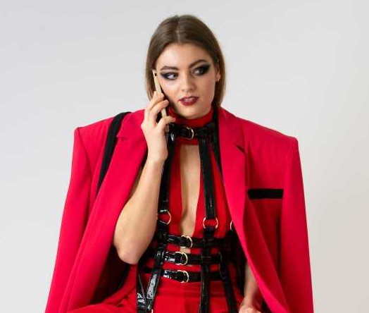 Foto: telefonierende Person in komplett rotem Outfit sitzt auf Hocker (Fotoquelle: Sarah Oberkofler, Model: Xenia Mühle)