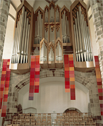Foto 1: Stoffbahnen hängen unter einer Kirchenorgel. Anja Spletzer - Textile Partituren – in Farbklängen gewebt – ein Raumobjekt