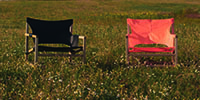 Foto: zwei Stühle auf einer Wiese, einer mit roter Sitzfläche und einer mit schwarzer Sitzfläche
