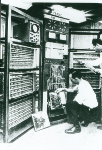 Foto: Ein Mann kniet vor dem alten Röhrenrechner TRADIC.