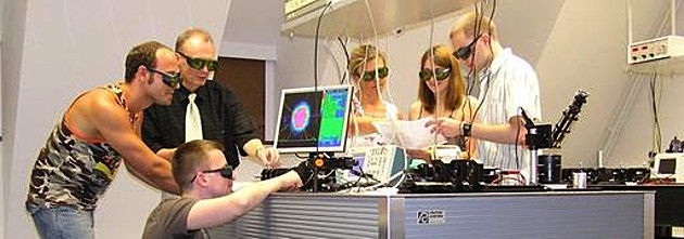 Foto zum Studiengang Mikrotechnologie. Sechs Studierende mit Schutzbrillen um einen Labortisch herum, lösen eine Aufgabe.