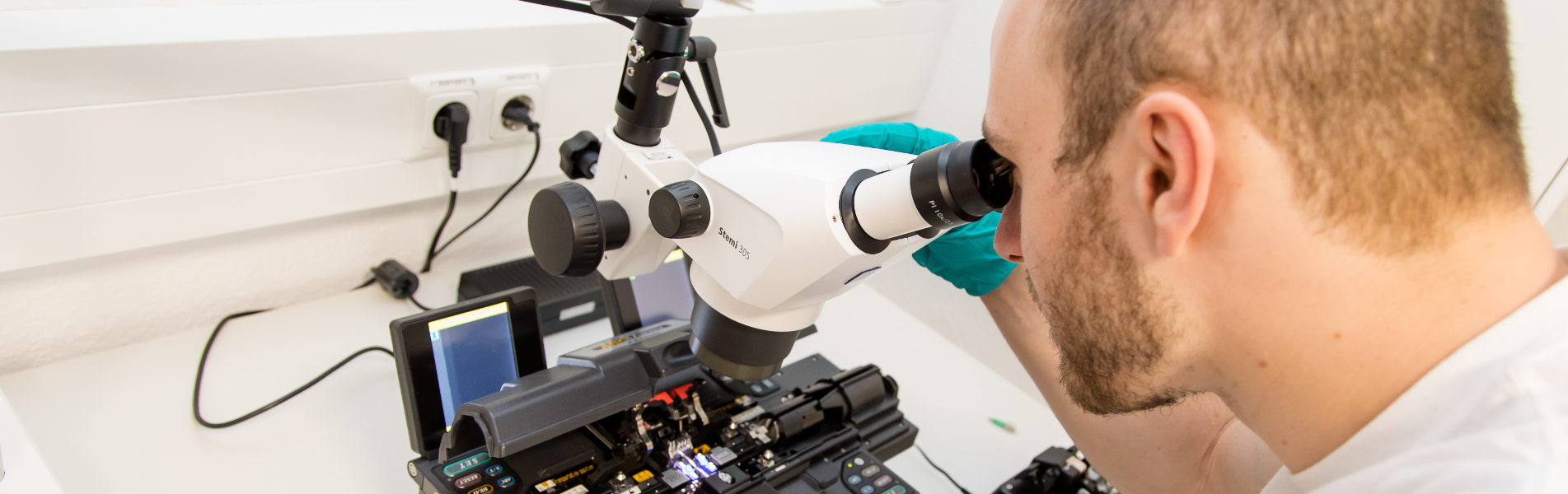 Foto: Ein Mitarbeiter schaut durch ein Mikroskop. Technische Kompetenzen am AZOM, Photonische Systeme, Fasertechnologien und Messtechnik, Oberflächen- und Werkstofftechnologien sowie Bildverarbeitung und Prozesskontrolle