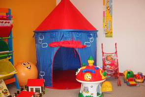 Foto: Ein Teil des Kinderbetreuungsraumes ist zu sehen. Verschiedenes buntes Spielzeug steht auf dem Boden.