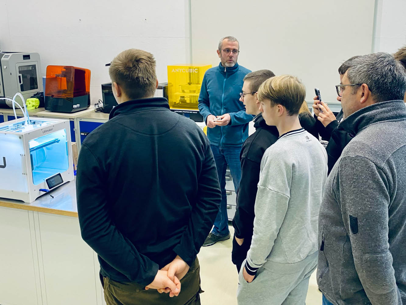 Schüler sehen sich einen 3-D-Drucker an, ein Labormitarbeiter erklärt dazu