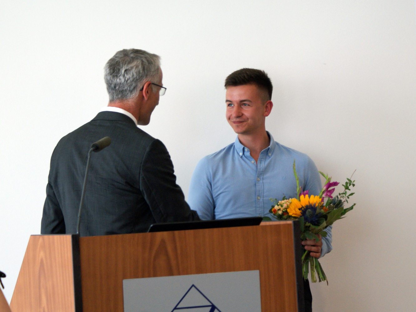 Dekan der AMB Prof. Dr.-Ing. Michael Kaiser gratuliert einem Absolventen mit hellblauen Hemd
