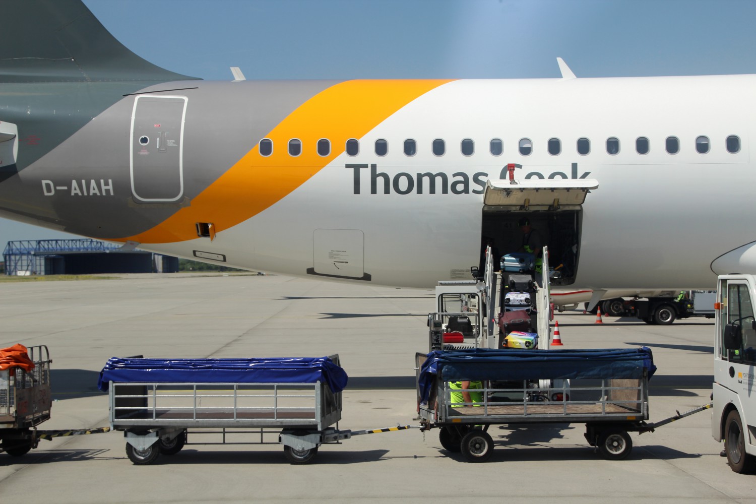 Foto: Heckansicht eines Flugzeuges was mit Gepäckstücken auf einer Rampe zur Ladeluke beladen wird. Davor stehen Kofferwagen.