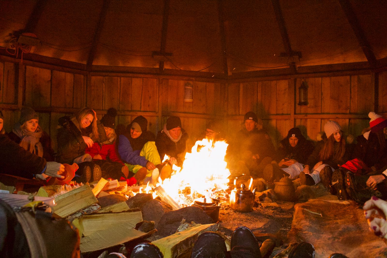 Foto: Eine Gruppe Studierender sitzen in einem Rundbauzelt um ein Lagerfeuer.