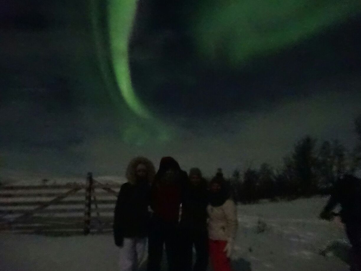 Foto: Vier Studierende stehen Abends in der Landschaft. Im Himmel sind Polarlichter zu sehen.