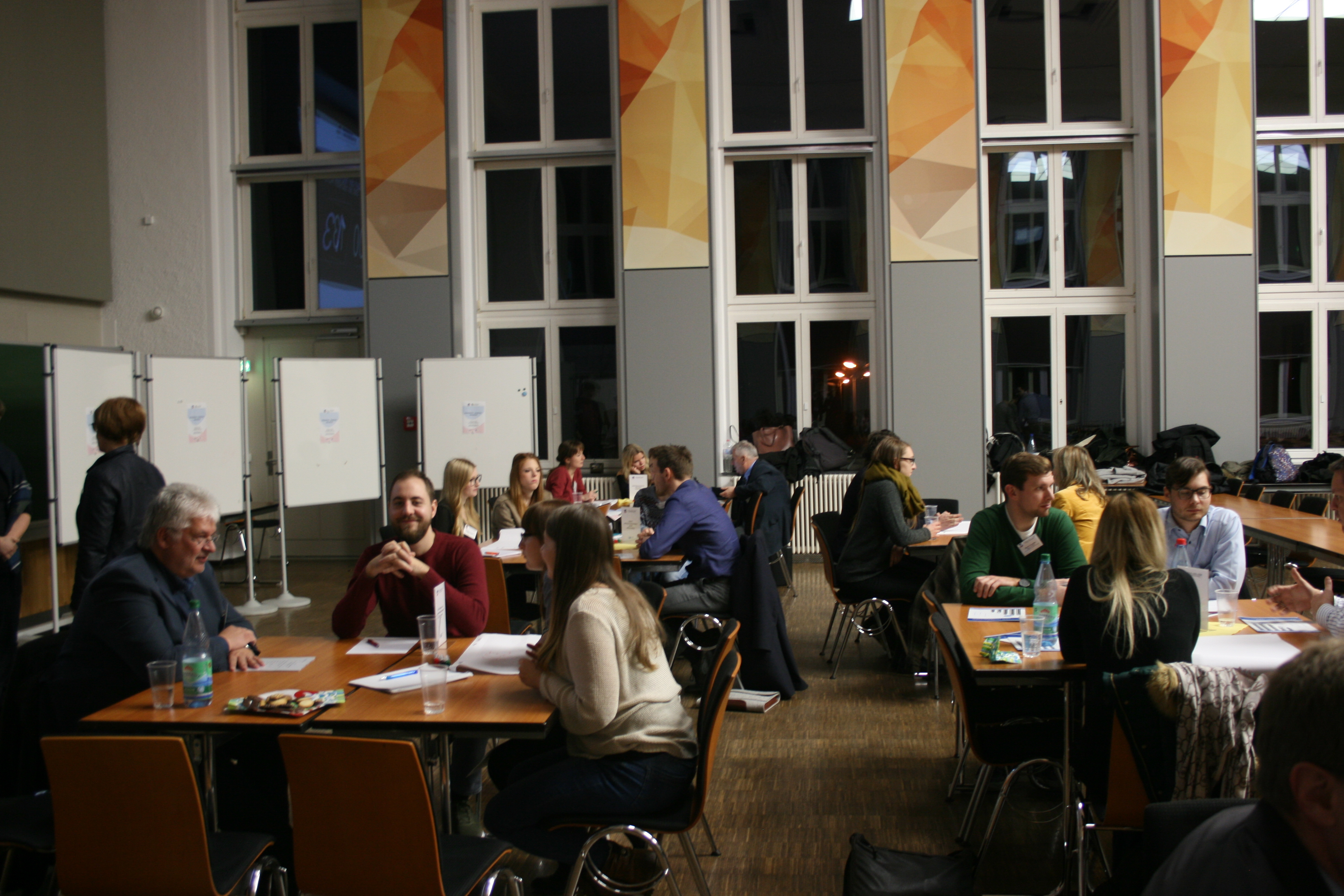 Foto: Unternehmer und Studentenstammtisch in der Aula Scheffelberg. Studierende und Unternehmensvertreter sitzen an verschiedenen Tischblöcken und tauschen sich untereinander aus.