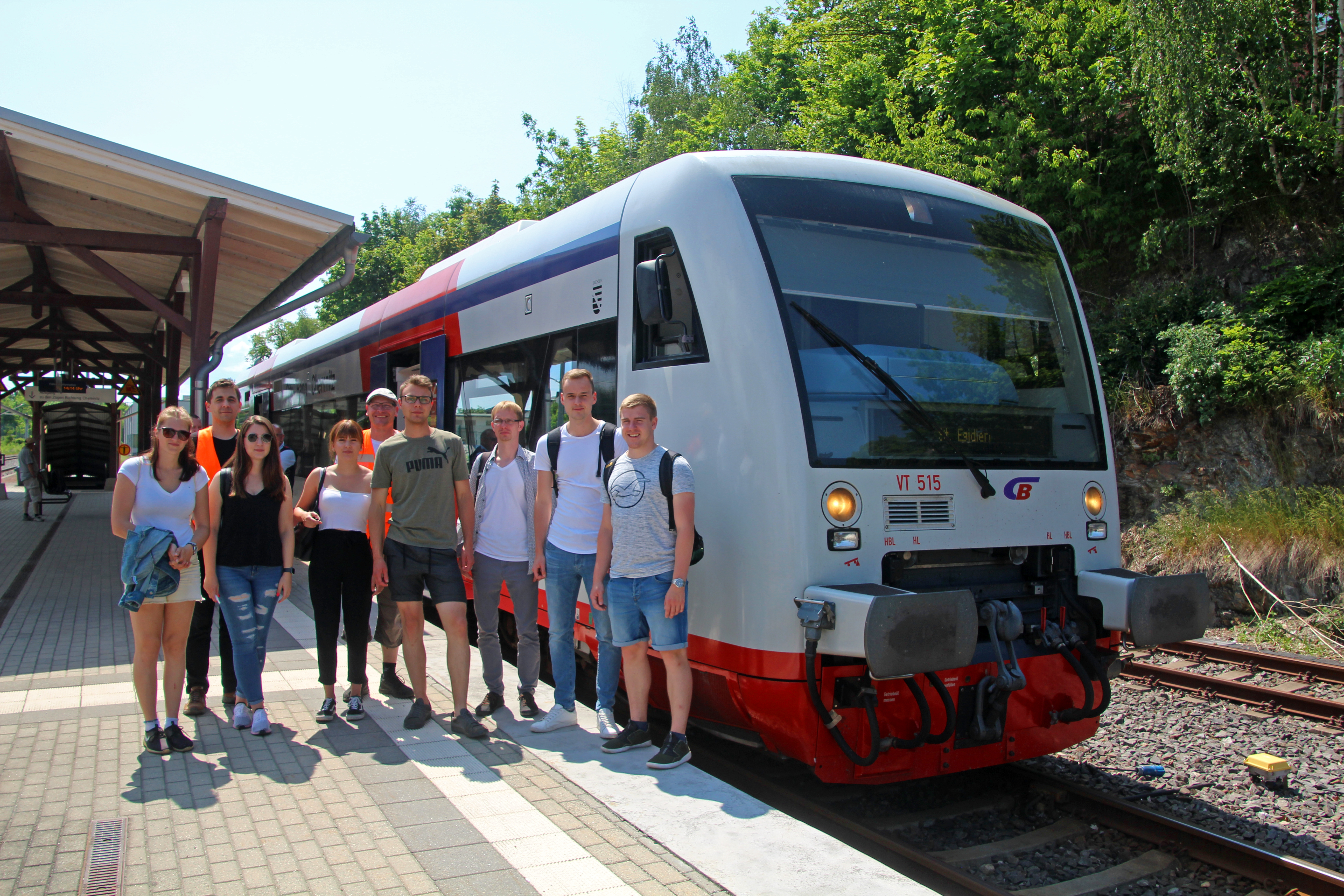 Gruppenfoto: Eine Gruppe Studierender steht auf einem Bahnsteig vor einem Triebwagen der Eisenbahn.