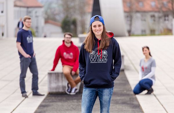 Foto: Eine Studierende steht auf dem Campus Scheffelberg und lächelt in die Kamera.