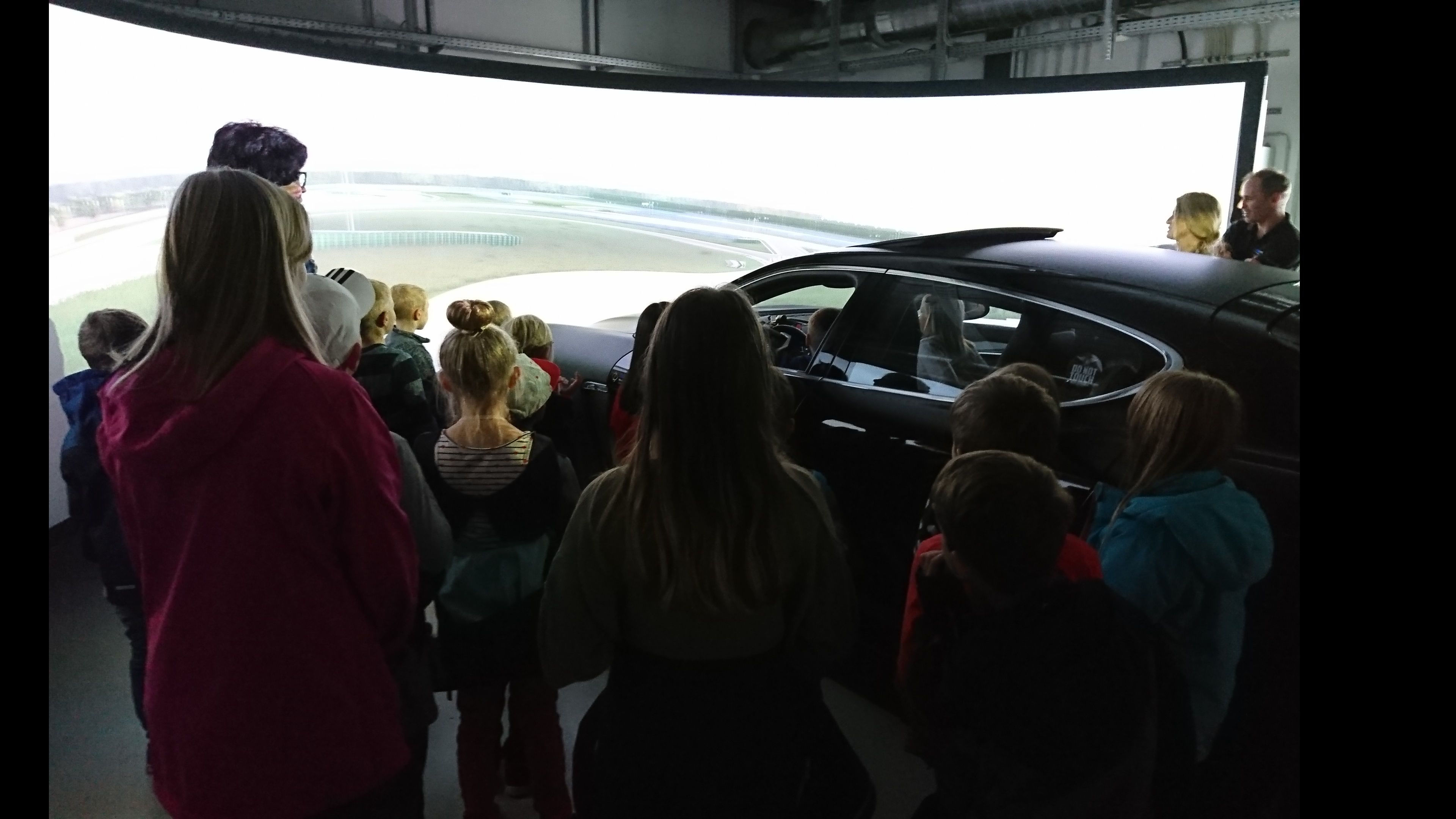 Foto: Besucher stehen im Fahrsimulationslabor um einen PKW mit einer großen Leinwand davor.