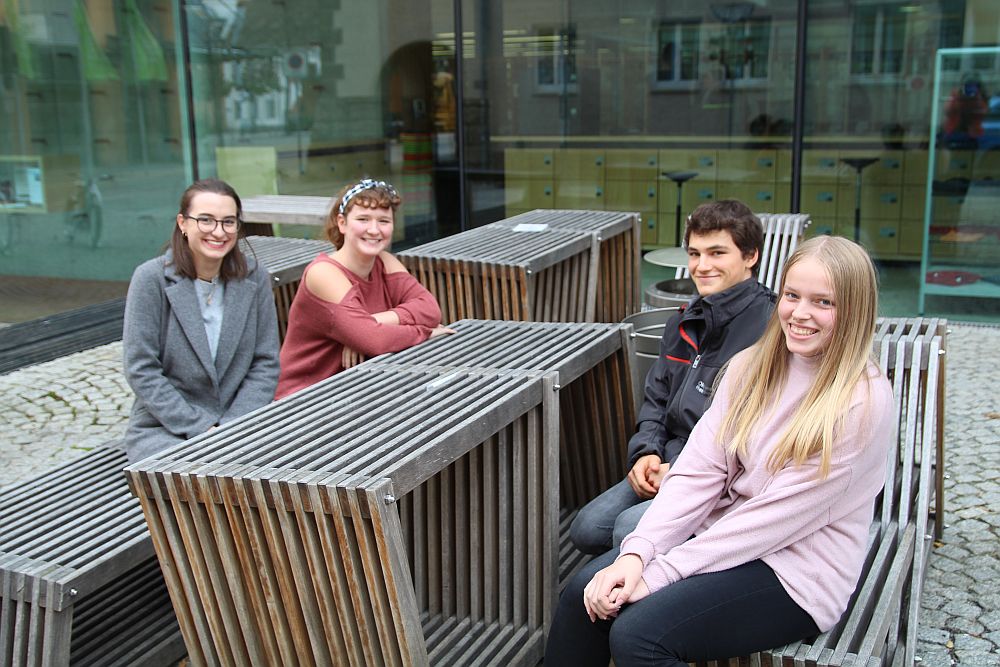 Foto: 4 Teilnehmer der Ferienuni sitzen vor der Hauptbibliothek an einem Tisch.
