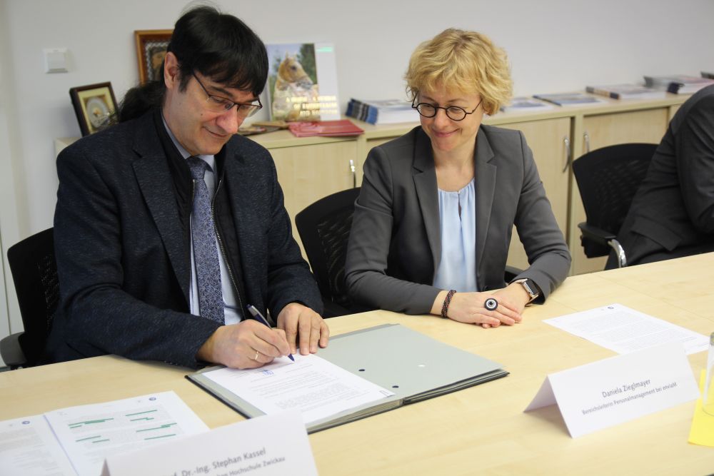 Foto: Rektor Kassel unterzeichnet eine Kooperationsvereinbarung. Daneben sitzt eine Frau.